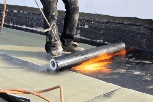 Roofer applying torch-on felt to flat roof using blowtorch - flat roofing installation