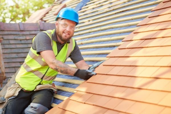 Roofer in hi-vis vest and blue hard hat installing new roof tiles