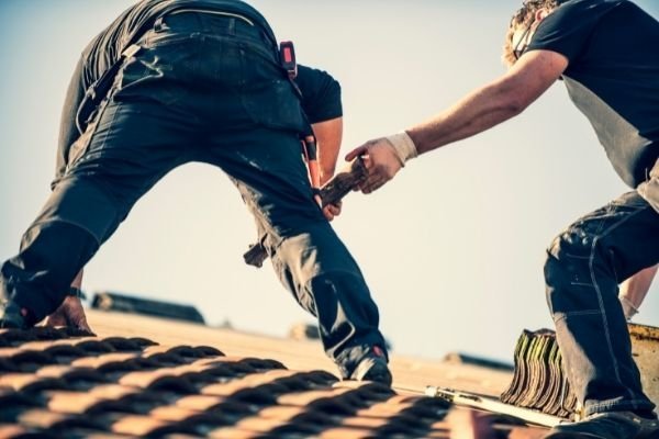 Two roofers repairing dark tiled pitched roof - professional roof repairs