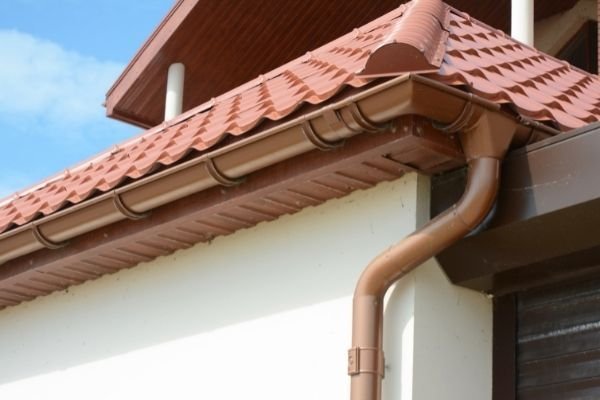 Close-up of red tiled roof with brown guttering, fascia and downpipe - roofline services